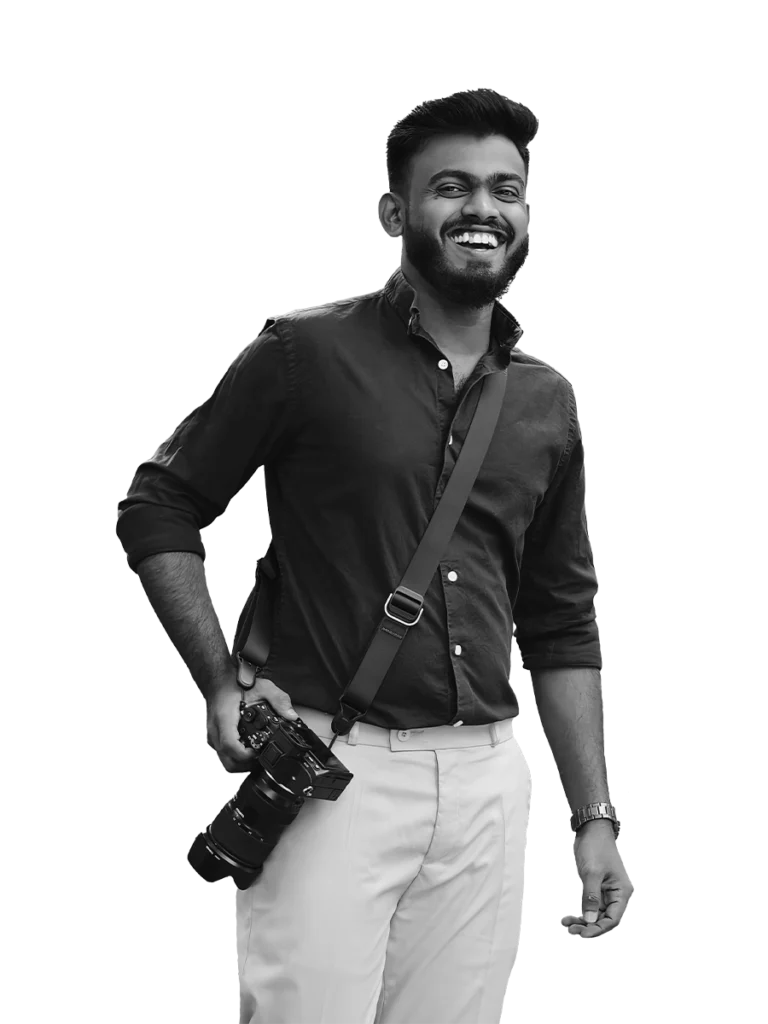 A portrait of a Pune-based photographer standing with a warm smile, holding his camera in front of him. His friendly demeanor and passion for photography are evident, inviting viewers to engage with his work