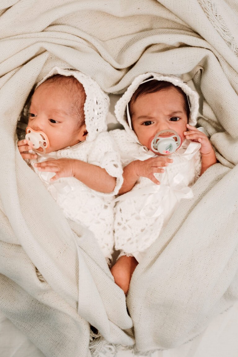 Candid picture of twin newborn children covered in a white cloth shaped like a heart.