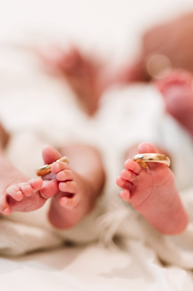 Cute legs of twin newborn children with their parents' wedding rings delicately hanging on their tiny fingers.