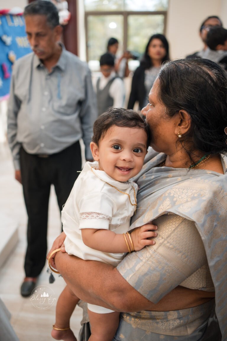 Baby joyfully smiling at the camera during his baptism ceremony.