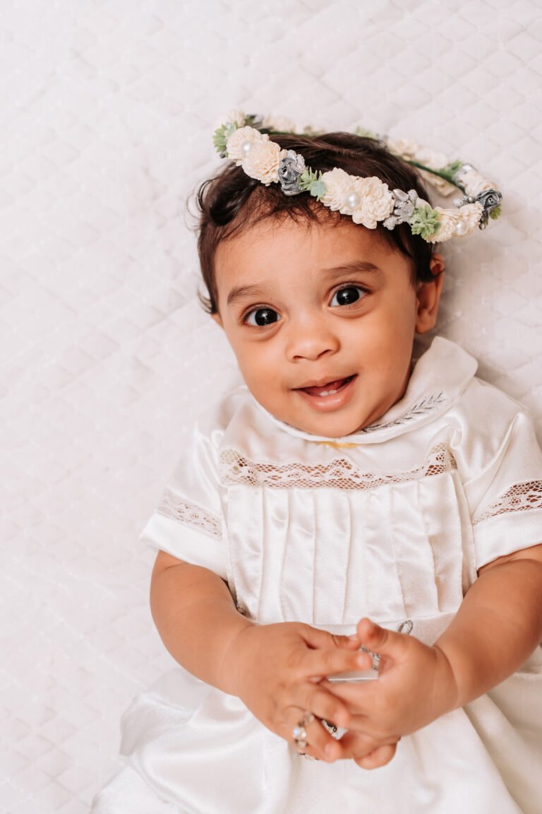 Cute baby portrait captured on baptism day morning. Baby is wearing a tiara/crown and smiling.