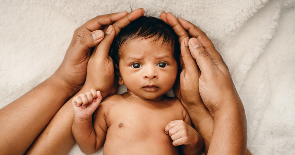 A close-up image captured of a baby surrounded by his parent's hands.