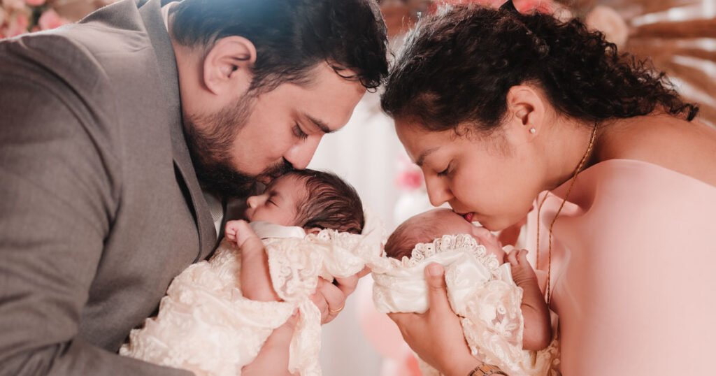 A close-up image of a mother and father holding and kissing their twin children on their baptism day.