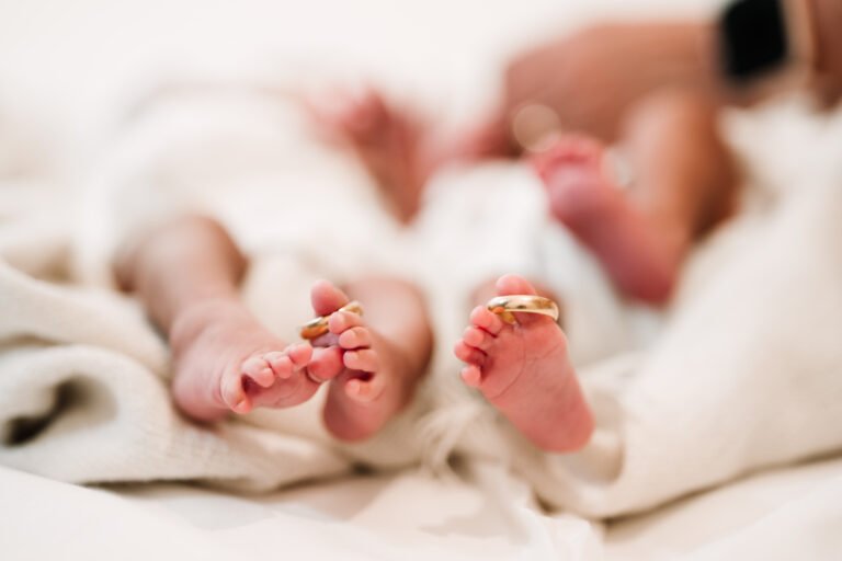 Cute legs of twin newborn children with their parents' wedding rings delicately hanging on their tiny fingers.