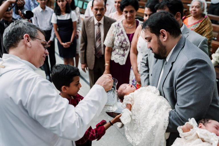 The priest baptizing a newborn baby by pouring water on her head, capturing a sacred and traditional moment during the baptism ceremony.