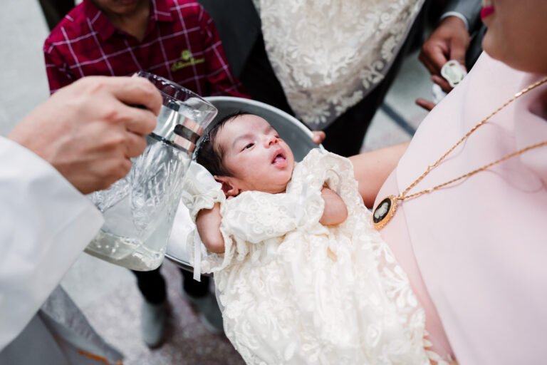 The priest baptizing a newborn baby by pouring water on her head, capturing a sacred and traditional moment during the baptism ceremony.