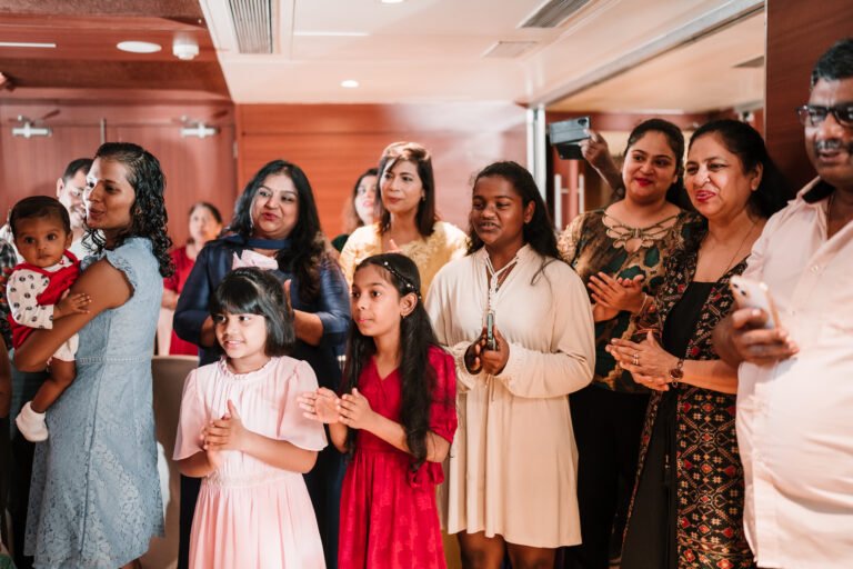 A crowd cheering during a cake cutting ceremony at the baptism celebration, capturing joyful and celebratory moments.