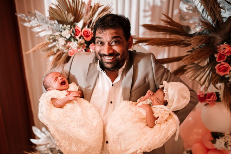 The uncle of the twins cheerfully holding twin babies, capturing a fun and loving candid moment